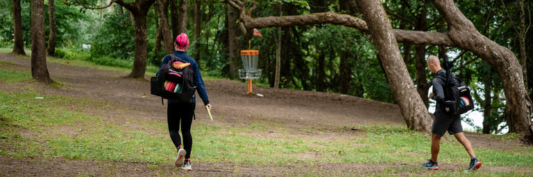 Disc golfere der går med deres tasker forbi en gul disc golf kurv