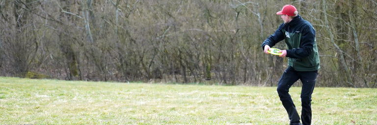 Disc golfer i grøn jakke der gør klar til at kaste baghåndskast med driver