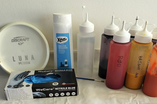 Udstyr til disc dye: en hvid disc, flasker med farve, handsker og en pensel
